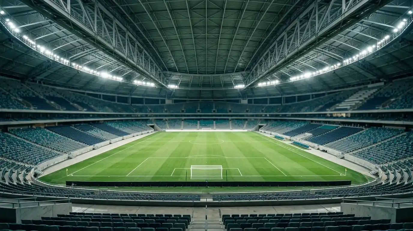 Weitwinkelaufnahme eines großen überdachten Fußballstadions von innen bei Flutlicht, leerer grüner Rasen, geschlossenes Dach, warme Beleuchtung