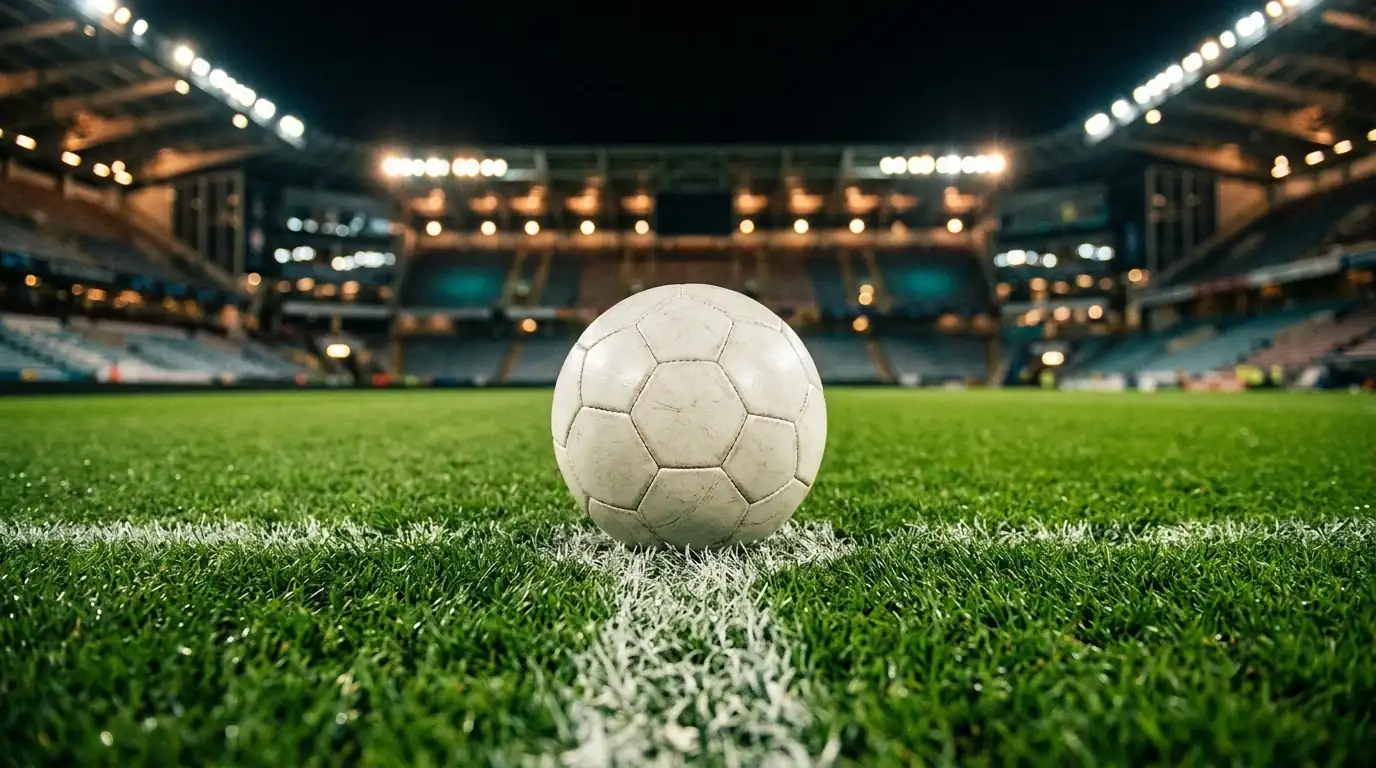 Nahaufnahme eines Fußballs auf dem Anstoßpunkt in einem hell erleuchteten Stadion bei Nacht, leere Tribünen im Hintergrund unscharf